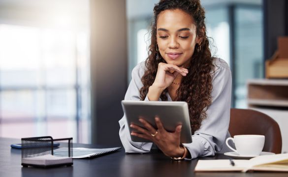 Imagem de mulher em uma mesa utilizando tablet com uma xícara ao lado